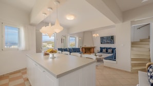 A spacious living area with a large island, a fireplace, and a view of the outdoors. - Rodanthi Hospitality (Faistos)