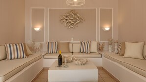 A modern living room with a sofa set, a coffee table with a bottle and glass, decorative wall art, and wall-mounted lighting. - Rodanthi Hospitality (Faistos)