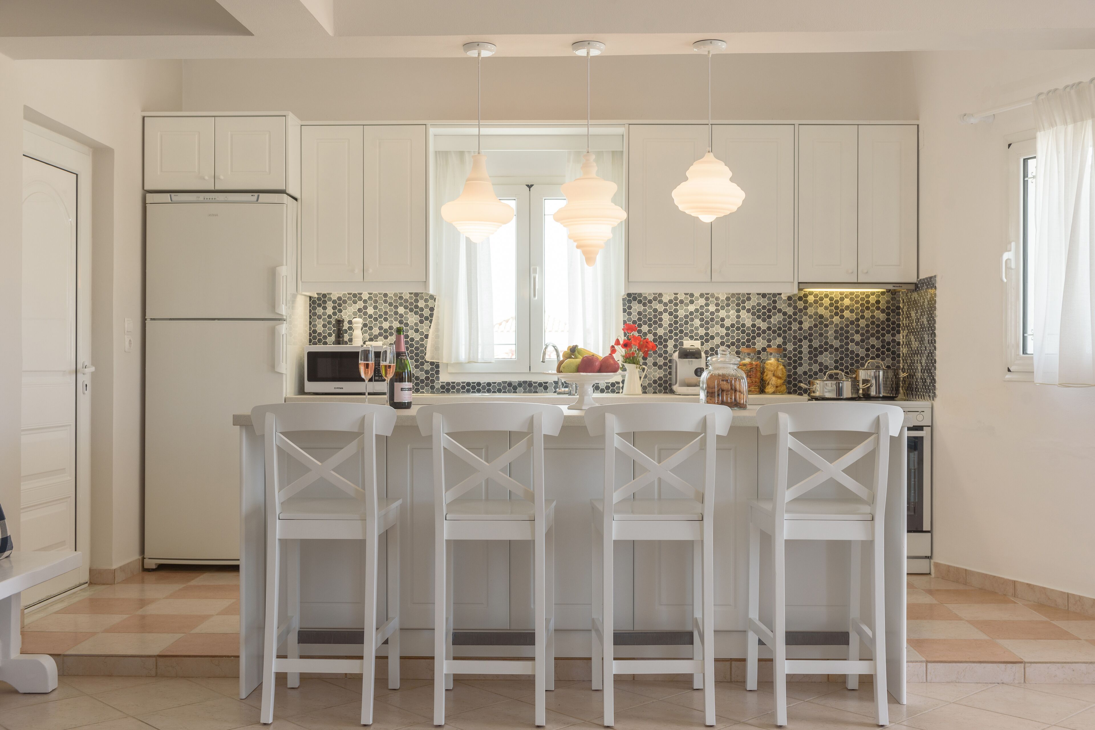 A modern kitchen with white cabinetry, a central island with bar stools, pendant lighting, and a tiled backsplash.