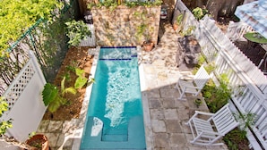 Une piscine rectangulaire bordée de carreaux, entourée d’une terrasse en pierre, d’une clôture blanche et de divers pots de plantes.