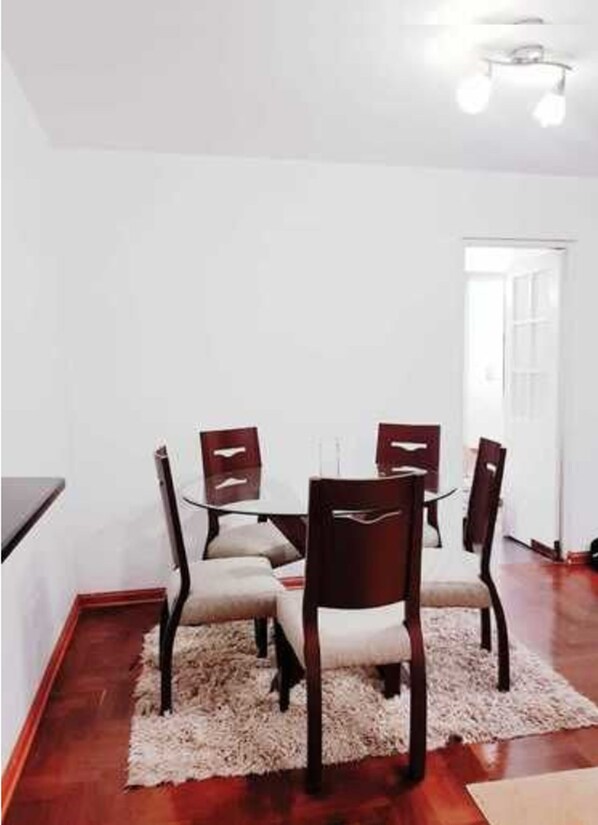 A dining area with a round table and four chairs, a white wall, and a wooden floor.