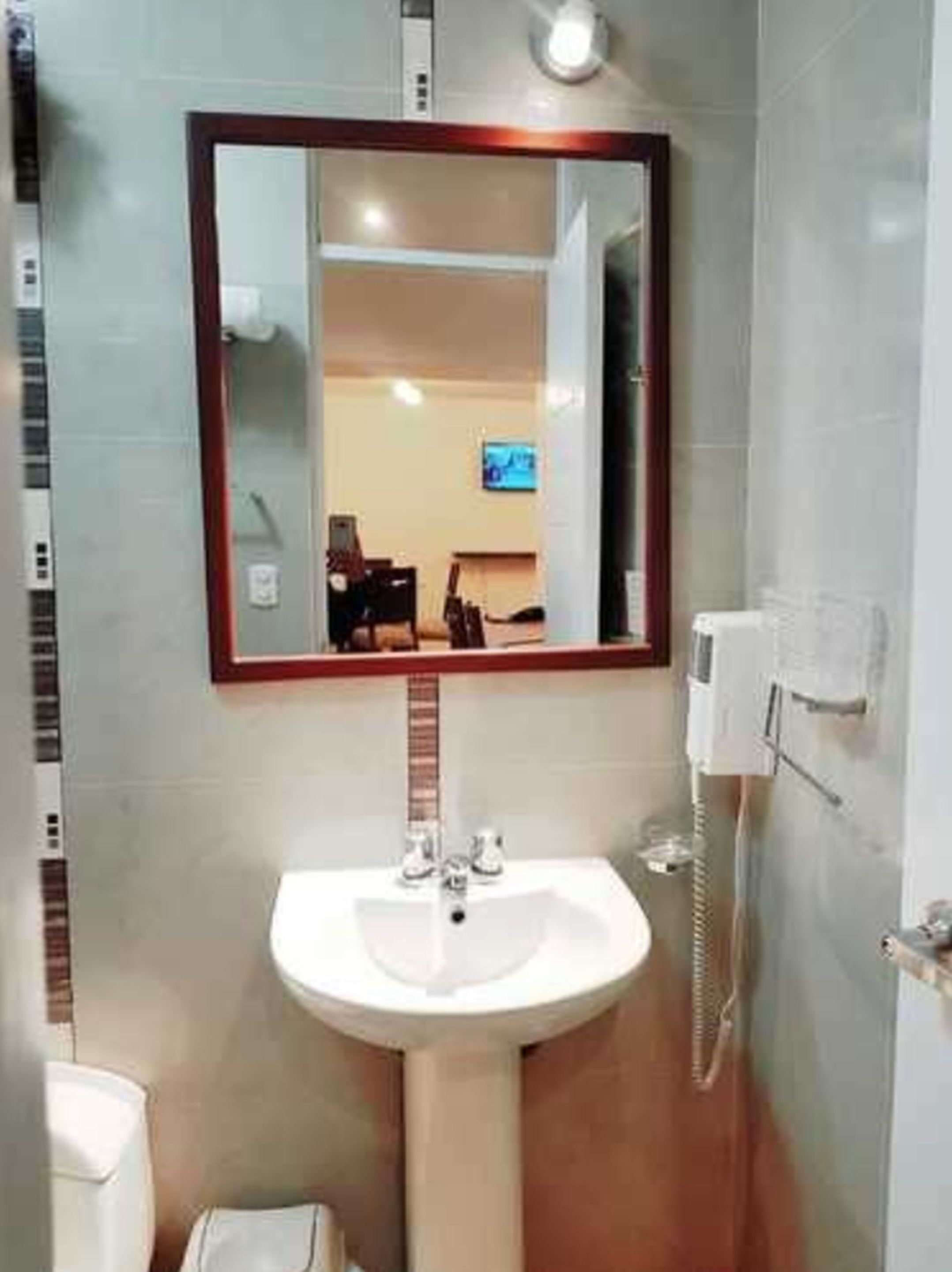 A bathroom with a sink, mirror, and a hairdryer on the wall.