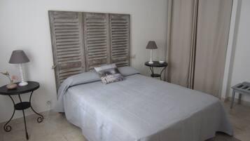 A neatly made bed with a grey bedspread and pillows, two bedside tables with lamps, a wooden headboard, and a chandelier.