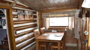 A rustic wooden cabin interior with a dining table, chairs, a window with curtains, and a wooden ceiling. - Historic Moose Lodge Cabin (South Fork)
