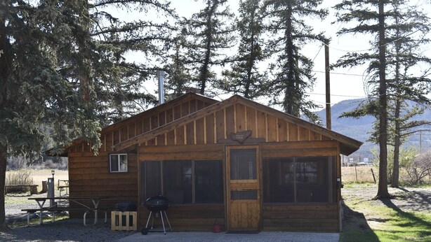 A rustic wooden cabin with a large window, a door, and a picnic table with a grill outside. - Historic Moose Lodge Cabin (South Fork)