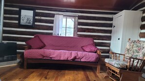 A log cabin interior with a wooden floor, a sofa, a chair, and a wardrobe. - Historic Moose Lodge Cabin (South Fork)
