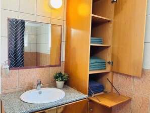 Une salle de bain avec un lavabo, un miroir et un meuble en bois doté d’étagères.