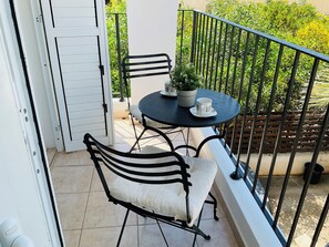 Un balcon avec une table ronde, deux chaises, une plante en pot et une porte blanche.