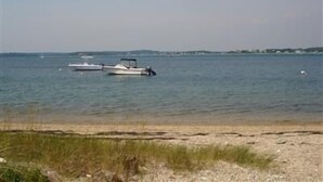 Une plage avec deux bateaux ancrés dans une eau calme, un ciel dégagé et une terre lointaine à l’horizon.