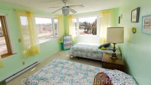 Une chambre avec deux lits, un ventilateur de plafond, une commode et une fenêtre avec des rideaux.