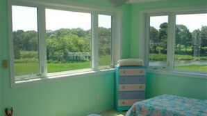 Une chambre avec deux lits, une commode et de grandes fenêtres donnant sur un paysage verdoyant.
