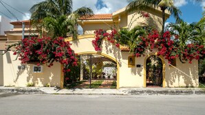 A yellow building with a red-tiled roof, surrounded by palm trees and red flowers. - Deep Blue Condo 102 by Skyrun (Isla Mujeres)