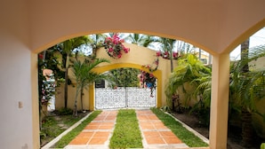A paved pathway leading to a gated entrance with a yellow archway, surrounded by greenery and flowering plants. - Isla 33 2BD Villa 1101 by Skyrun (Isla Mujeres)