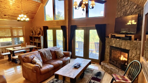 A spacious living room with a leather sofa, wooden coffee table, and a stone fireplace. - Mtn Views/Large Master Suite/Hot Tub/Wi-Fi (Bryson City)