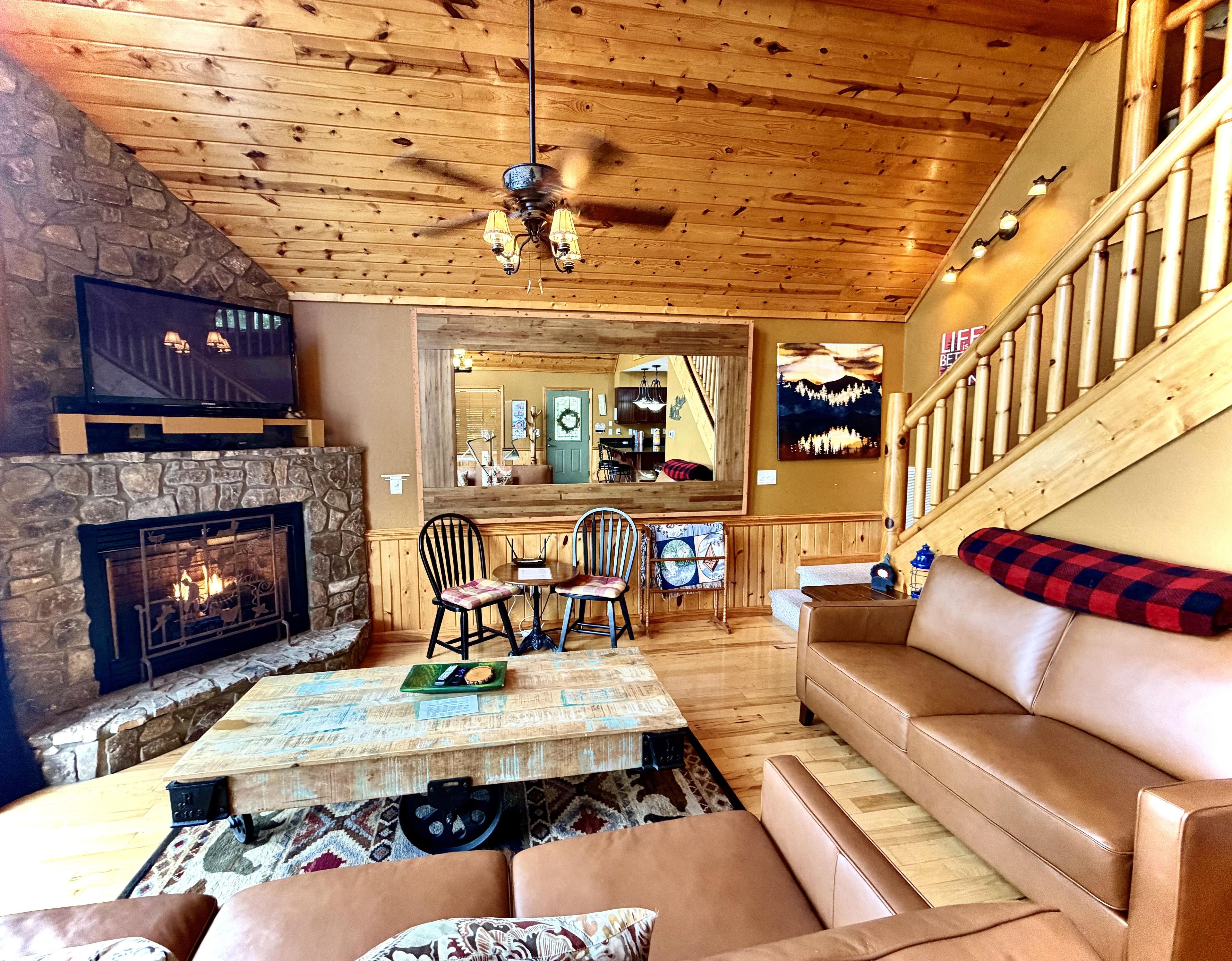 A cozy living room with a stone fireplace, a wooden ceiling, a sofa, and a dining area with chairs.