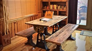 A wooden dining table with benches, a bookshelf with books, a decorative wall piece, and a window with blinds. - Mtn Views/Large Master Suite/Hot Tub/Wi-Fi (Bryson City)