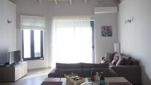 A living room with a sofa, a coffee table, a TV, and a window with curtains. - Villa Mons & Mare (Igoumenitsa)