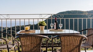 A round glass table with wicker chairs on a balcony overlooking a mountainous landscape. - Villa Mons & Mare (Igoumenitsa)