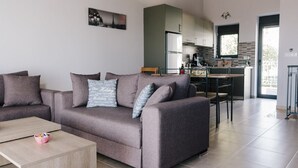 A modern living room with a grey sofa, a wooden coffee table, and a kitchen in the background. - Villa Mons & Mare (Igoumenitsa)