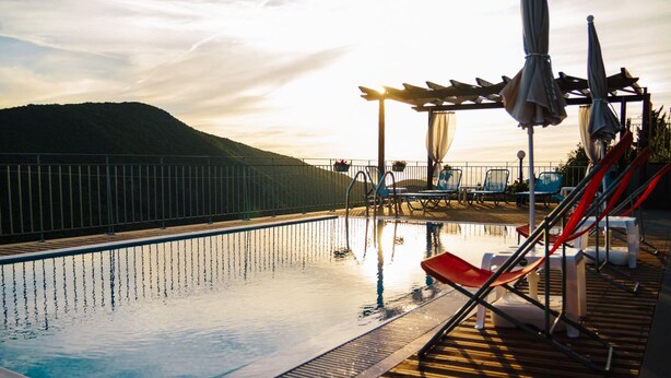 A pool area with lounge chairs and umbrellas, surrounded by a wooden deck and a metal railing. - Villa Mons & Mare (Igoumenitsa)