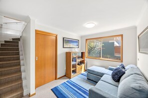 A modern living room with a staircase, a wooden door, a bookshelf, and a large window.