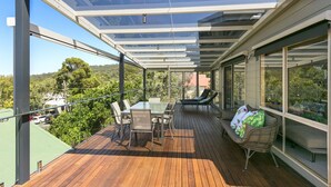 A modern outdoor deck with a glass ceiling, wooden flooring, and outdoor furniture. - Boston Beach House (Lorne)