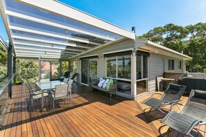 A covered outdoor deck with a glass enclosure, furnished with chairs and a table. - Boston Beach House (Lorne)