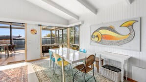 A spacious dining area with a large table and chairs, a view through glass doors, and a wall-mounted painting. - Boston Beach House (Lorne)