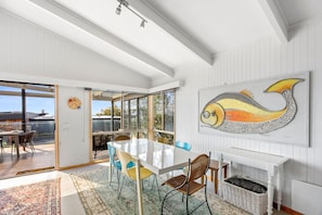 A spacious dining area with a large table and chairs, a view through glass doors, and a wall-mounted painting. - Boston Beach House (Lorne)