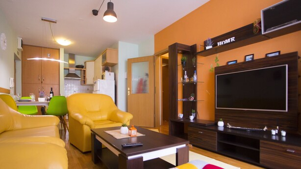 A modern living room with yellow leather sofas, a wooden coffee table, and a large flat-screen TV mounted on a wooden wall.