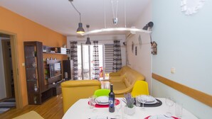 A dining area with a white table set for four, a sofa, and a TV in the background.