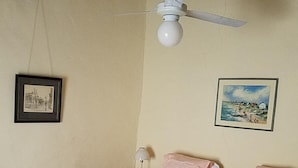 Une chambre à coucher comprenant un lit, une table de chevet, un ventilateur de plafond et deux tableaux encadrés accrochés au mur.