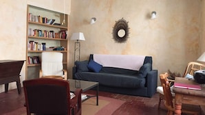 Un salon avec un canapé bleu foncé, une bibliothèque en bois, une table basse et un coin repas comprenant une table et des chaises en bois.