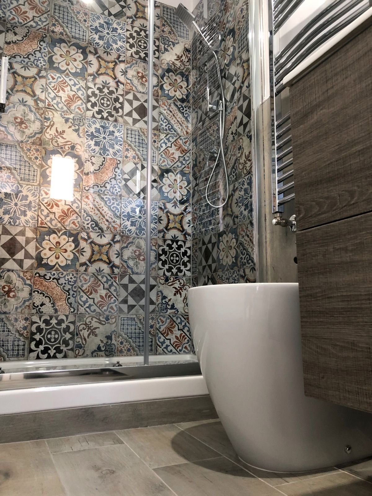 Une salle de bain équipée d’une douche, d’une baignoire et d’un mur recouvert de carreaux formant un motif géométrique.