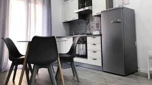 Eine moderne Küche mit Essbereich, ausgestattet mit einem Kühlschrank, Schränken und einem Esstisch mit Stühlen.