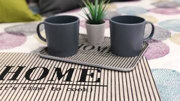 Eine Küchenecke mit zwei schwarzen Tassen auf einem Tablett, einer kleinen Topfpflanze und einer Unterlage mit dem Wort 'HOME' und dem Spruch 'Zeit zu kochen'.