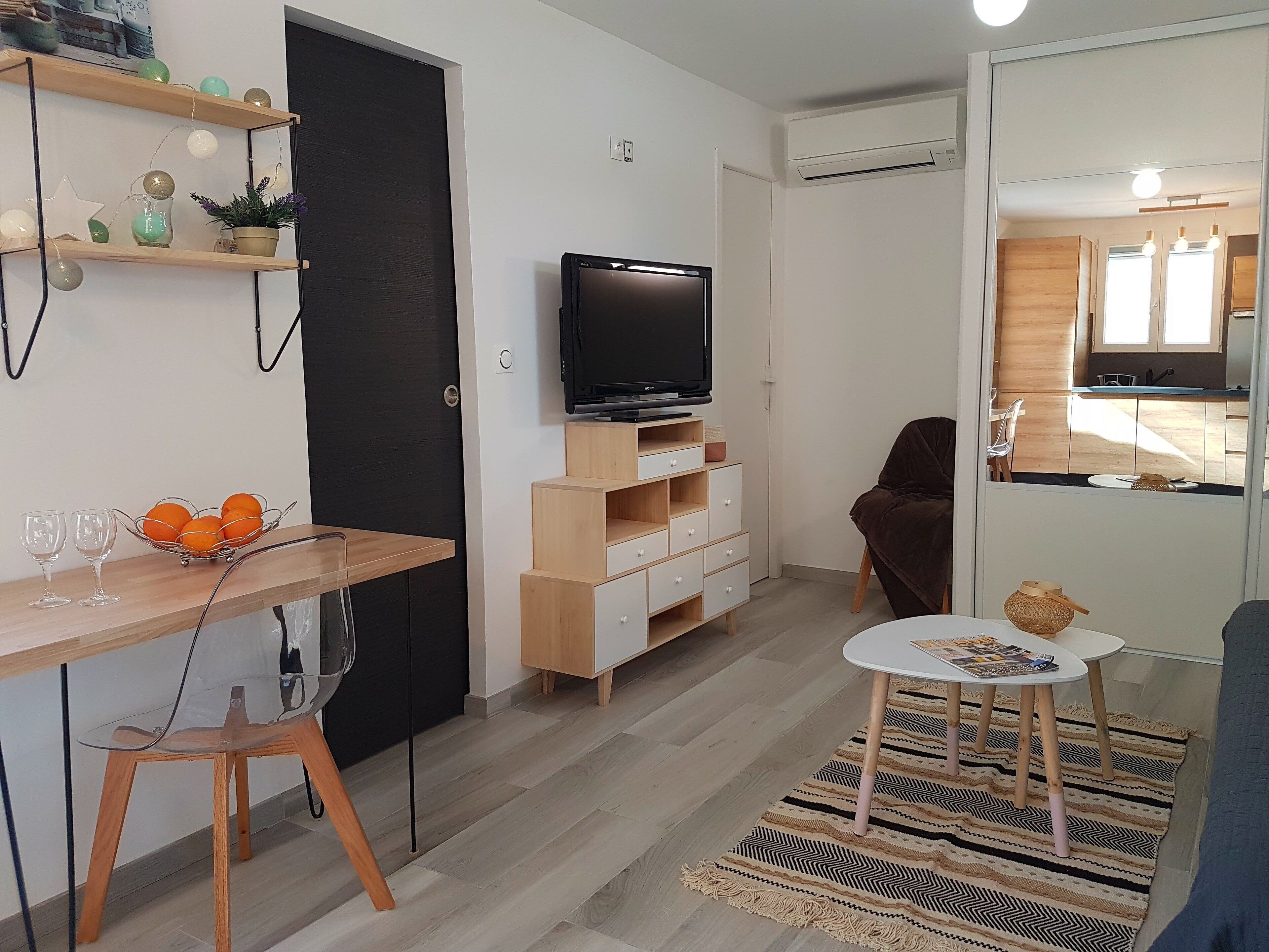 Een moderne woonkamer met een televisie, houten meubels, een eethoek en een keuken die door een open deur zichtbaar is.