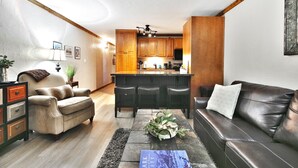 A modern living room with a leather sofa, a coffee table, and a kitchen area with wooden cabinets and a bar.