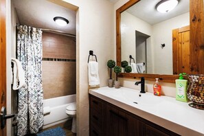 A bathroom with a bathtub, toilet, and a sink with a mirror. There are two bottles of hand soap on the sink.