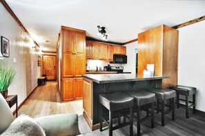 A kitchen with wooden cabinets, a microwave, a sink, and a bar area with stools.