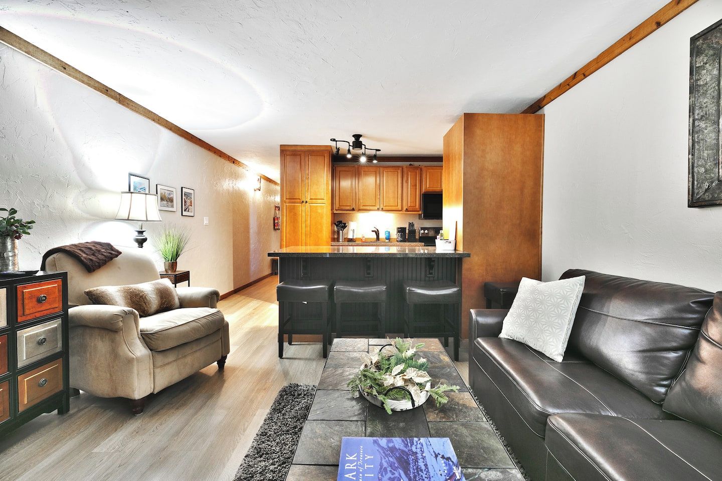 A modern living room with a leather sofa, a coffee table, and a dining area with wooden cabinets and a bar.