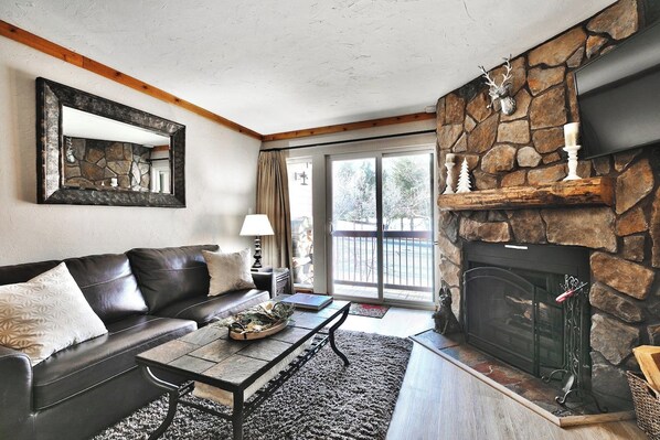 A living room with a stone fireplace, a leather sofa, and a large window.