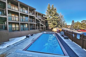 A multi-story building with a swimming pool, outdoor seating, and a wooden fence.