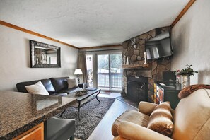 Una sala de estar con chimenea de piedra, un sofá, una mesa de centro y un televisor montado en la pared.