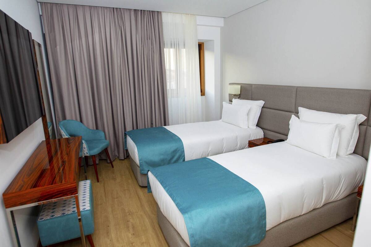 A hotel room with two beds, a desk, a chair, and a window with curtains.