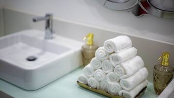 A bathroom sink with a gold tray holding rolled white towels and two gold-scented bottles.