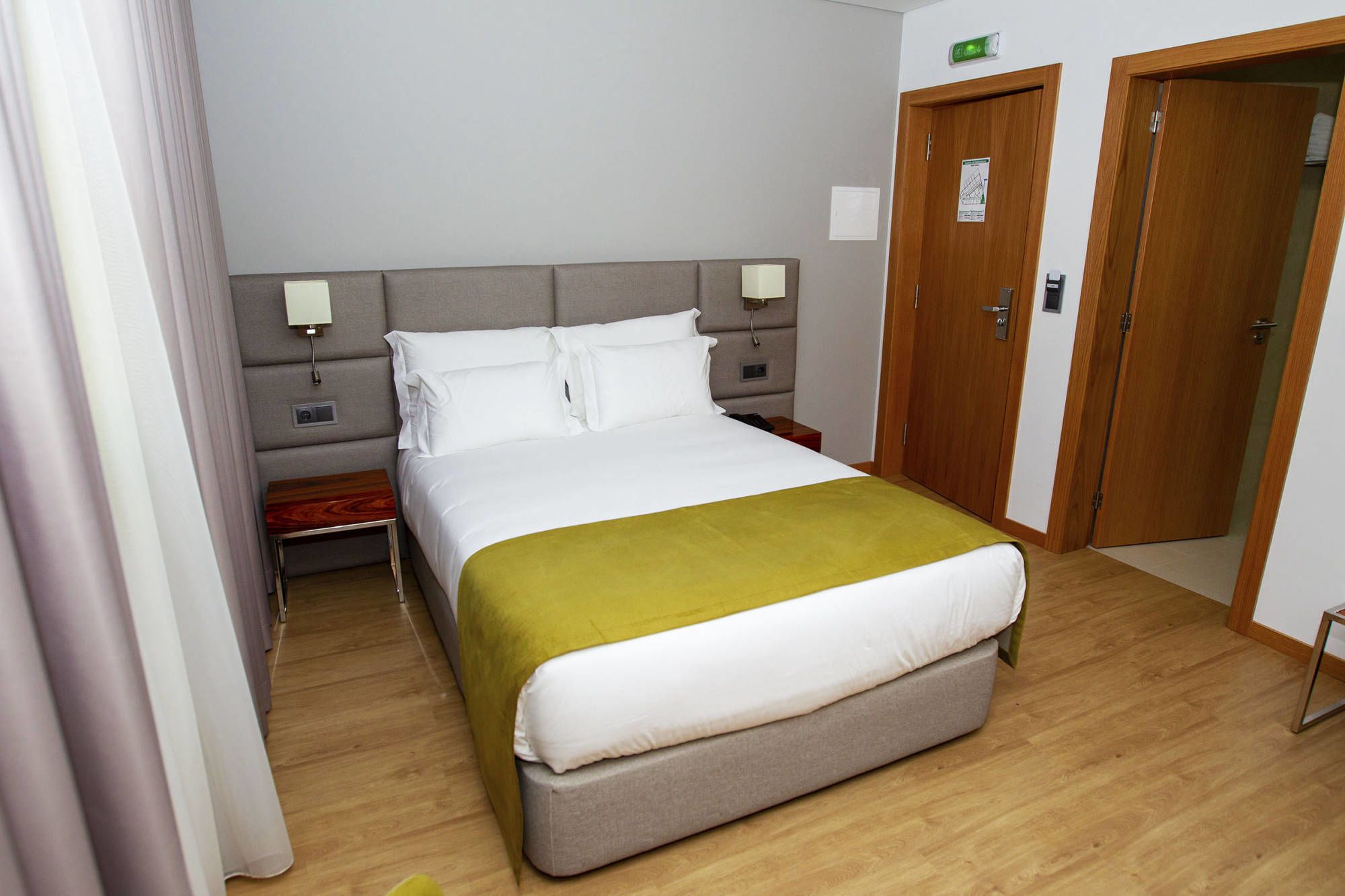 A hotel room with a bed, bedside tables, a nightstand, a wardrobe, and a door.