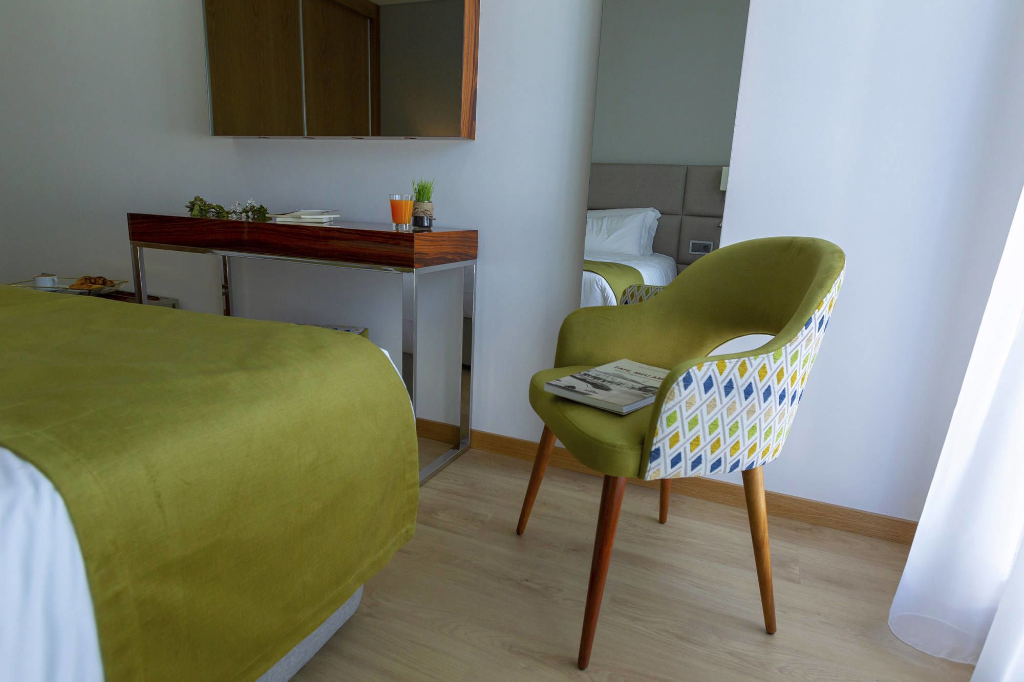 A hotel room with a bed, a desk, a chair, and a mirror.