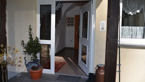 En byggnadsentré med nummer 134 ovanför dörren, en krukväxt, en kattstaty och ett fönster med gardiner.