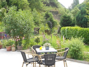 Eine Gartenpatio mit Korbmöbeln und einem Tisch, umgeben von üppigem Grün und verschiedenen Pflanzen.
